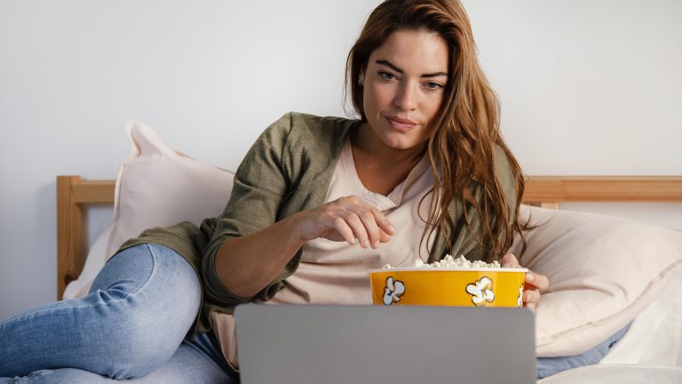 woman eating popcorn while watching movie laptop