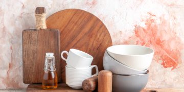 top-view-oil-bottle-stacked-pots-grater-wooden-cutting-board-colorful-surface
