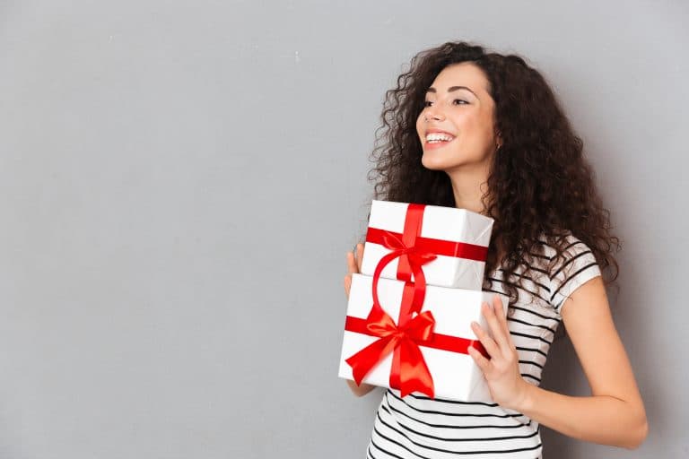half turned photo gorgeous female striped t shirt holding two gift wrapped boxes with red bows being excited joyous grey wall